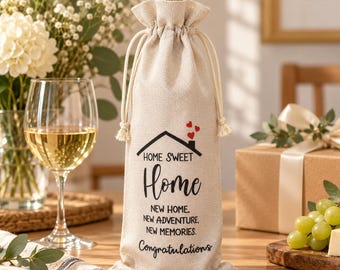 May include: A beige fabric wine bottle gift bag with a drawstring closure. The bag features a black graphic of a house with three small red hearts above it, and the text: HOME SWEET Home, NEW HOME. NEW ADVENTURE. NEW MEMORIES. Congratulations.