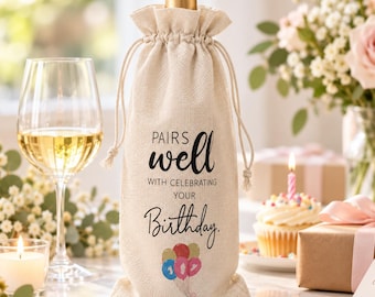 May include: A beige fabric wine bottle gift bag with a drawstring closure. The bag features black text that reads "PAIRS well WITH CELEBRATING YOUR Birthday." Below the text is a colorful illustration of five balloons in red, yellow, blue, and pink.