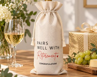 May include: A beige linen wine bottle gift bag with a drawstring closure. The text printed on the front reads PAIRS WELL WITH Retirement in black and red lettering, with a small red heart icon and the word CONGRATULATIONS below it.