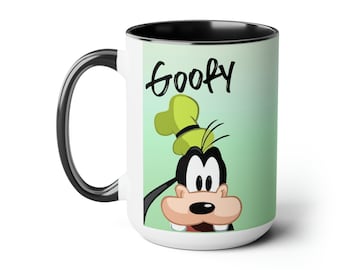 May include: White ceramic coffee mug with a black rim and handle. The mug features a cartoon image of Goofy with the word "Goofy" written in black above him. The background is a light green gradient.