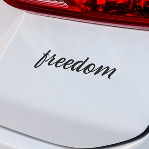 以下が含まれることがあります： 白い車のリアバンパーに黒い「freedom」のステッカーが貼ってある