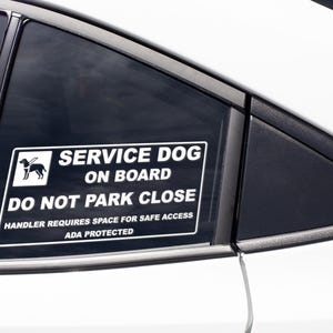Peut inclure: Un autocollant rectangulaire blanc sur une vitre de voiture indique "SERVICE DOG ON BOARD DO NOT PARK CLOSE". Il comprend un dessin de chien et le texte "HANDLER REQUIRES SPACE FOR SAFE ACCESS ADA PROTECTED."