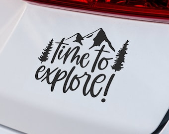 May include: Black vinyl decal with the words "time to explore!" in a handwritten font, with mountain and tree silhouettes. The decal is applied to a white surface, likely a car.