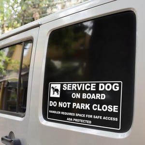 May include: A white rectangular sticker on a car window with black text that reads "SERVICE DOG ON BOARD DO NOT PARK CLOSE". The sticker also includes the text "HANDLER REQUIRES SPACE FOR SAFE ACCESS ADA PROTECTED". A silhouette of a dog is also included.