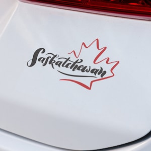 May include: A white car with a red, white, and black sticker that says "Saskatchewan" with a red maple leaf design.