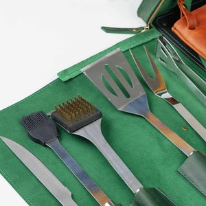 Op de afbeelding: Een groene leren rolhoes met een set grillgereedschap. De gereedschappen omvatten een spatel, tang, grillborstel, bestrijkborstel en een mes. De hoes is gesloten en de gereedschappen zijn zichtbaar.