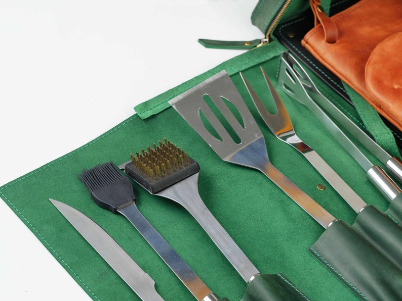 Op de afbeelding: Een groene leren rolhoes met een set grillgereedschap. De gereedschappen omvatten een spatel, tang, grillborstel, bestrijkborstel en een mes. De hoes is gesloten en de gereedschappen zijn zichtbaar.
