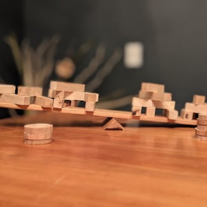 May include: A wooden seesaw with two stacks of wooden blocks on each end. The seesaw is balanced with the blocks on each side.