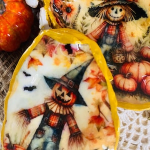 Puede incluir: Conchas de ostra pintadas a mano con temática otoñal. Cada concha presenta un diseño de espantapájaros con calabazas, hojas de otoño y murciélagos. Las conchas tienen un borde amarillo, ideales para la decoración de temporada.