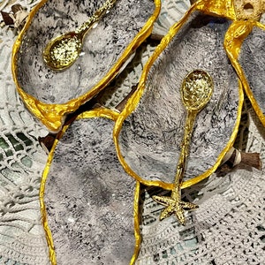 Puede incluir: Tres cuencos peque&ntilde;os de cer&aacute;mica gris y blanca con bordes dorados. Cada cuenco tiene una cuchara dorada con un mango en forma de estrella de mar.