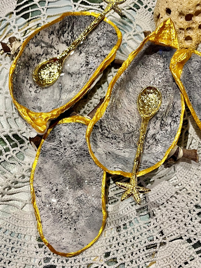 Puede incluir: Tres cuencos peque&ntilde;os de cer&aacute;mica gris y blanca con bordes dorados. Cada cuenco tiene una cuchara dorada con un mango en forma de estrella de mar.