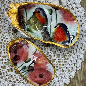 May include: Two decorative seashell dishes with gold trim. One dish features a watercolor painting of two robins perched on a branch with red poppies in the background. The other dish features a watercolor painting of red poppies.