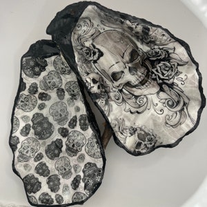 Peut inclure: Deux coquilles d'huîtres noires et blanches avec un motif décoratif. Une coquille présente un crâne avec des accents floraux et l'autre coquille a un motif répété de crânes de sucre.