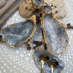 Puede incluir: Tres platos de concha de ostra grises y blancos con detalles dorados. Los platos est&aacute;n dispuestos sobre una superficie de crochet blanco. Dos cucharas doradas con mangos en forma de flor est&aacute;n en el plato m&aacute;s peque&ntilde;o.