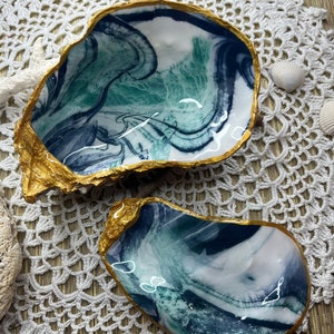 Peut inclure: Deux plats décoratifs en forme de coquille d'huître avec un design marbré bleu, vert et blanc. Les bords des coquilles sont peints en or.