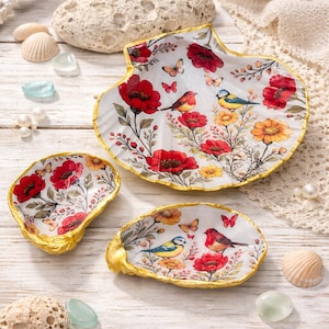 Peut inclure: Ensemble de trois plats décoratifs en forme de coquillage. L'intérieur blanc est orné d'un motif floral et d'oiseaux, avec des coquelicots rouges, des fleurs jaunes et des papillons. Les bords sont dorés.