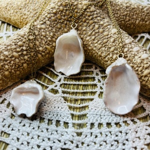 May include: Three white shell necklaces with gold chains. The shells are different sizes and are hanging from a starfish and a crocheted surface.
