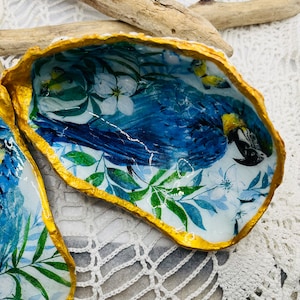 Può includere: Piatto decorativo a conchiglia di ostrica con un design di ara blu. L'interno presenta una stampa vibrante di un'ara blu in mezzo a fogliame tropicale e fiori bianchi. Il bordo è rifinito con vernice dorata. Un pezzo d'accento a tema costiero unico.