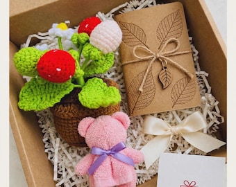 May include: A gift box containing a crocheted potted plant with red and white berries, a brown notebook with embossed leaf patterns tied with twine and a leaf charm, a small pink towel bear with a purple ribbon, and a white thank you card.