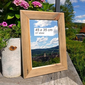 May include: A rectangular mirror with a light brown natural wood frame featuring visible grain and knots. The mirror surface reflects a blue sky with clouds and a town landscape. Text on the mirror reads 45 x 35 cm and ST 4544.