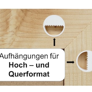 May include: A light-colored wooden frame corner featuring two white circular sawtooth hangers attached to the wood. A white rectangular label with black text reads: Aufh&auml;ngungen f&uuml;r Hoch &ndash; und Querformat. Two black arrows point to the hangers.