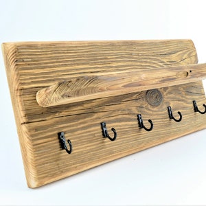 Könnte beinhalten: Rustikaler Schlüsselhalter aus Holz mit einem Regal und fünf schwarzen Metallhaken. Das Holz hat eine natürliche, gewitterte Oberfläche.