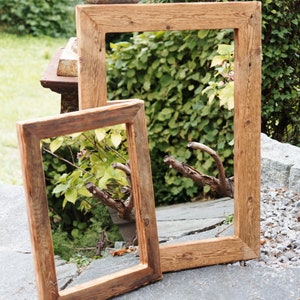 May include: Two rectangular picture frames made of natural brown wood with visible grain and knots. The frames are empty, featuring mitered corners and a simple, flat profile. They are positioned upright, with the smaller frame overlapping the larger one.