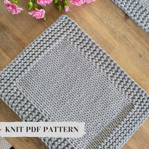 Può includere: Un sottopentola quadrato di maglia grigia con un motivo testurizzato. Il sottopentola ha un bordo attorno ai bordi. Il testo "KNIT PDF PATTERN" è stampato sul fondo del sottopentola.