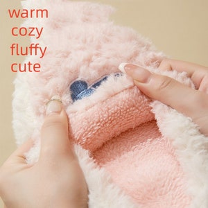 May include: A close-up of a pink and white fluffy item with the words "warm, cozy, fluffy, cute" in red. The item has a blue embroidered design. The inside is a soft pink material.