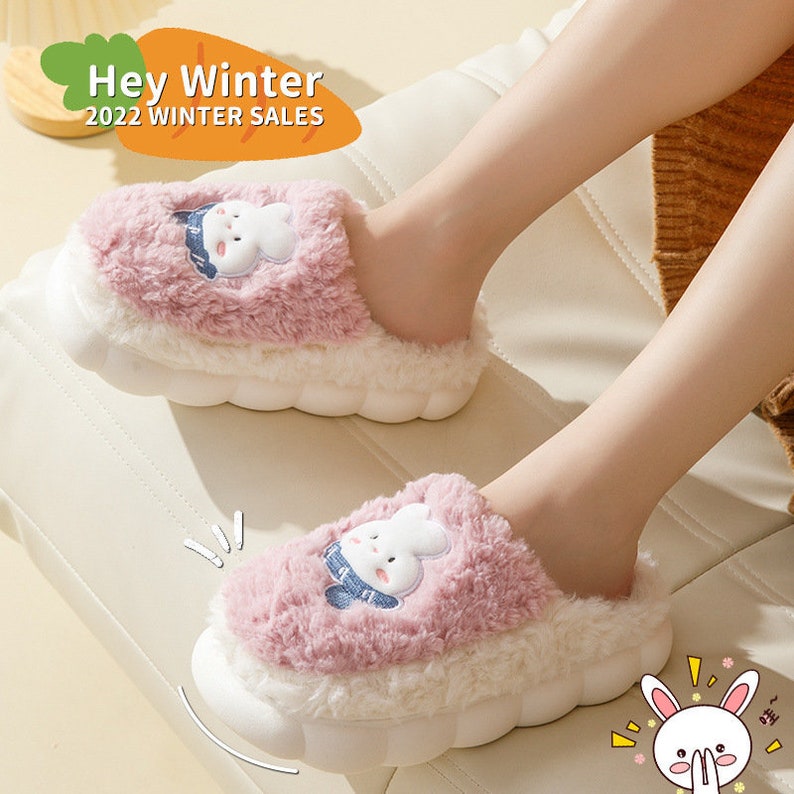 May include: Pink and white plush slippers with a cartoon bunny design. The slippers have a thick, white sole and a fluffy pink upper. The text "Hey Winter 2022 WINTER SALES" is in the upper left corner.