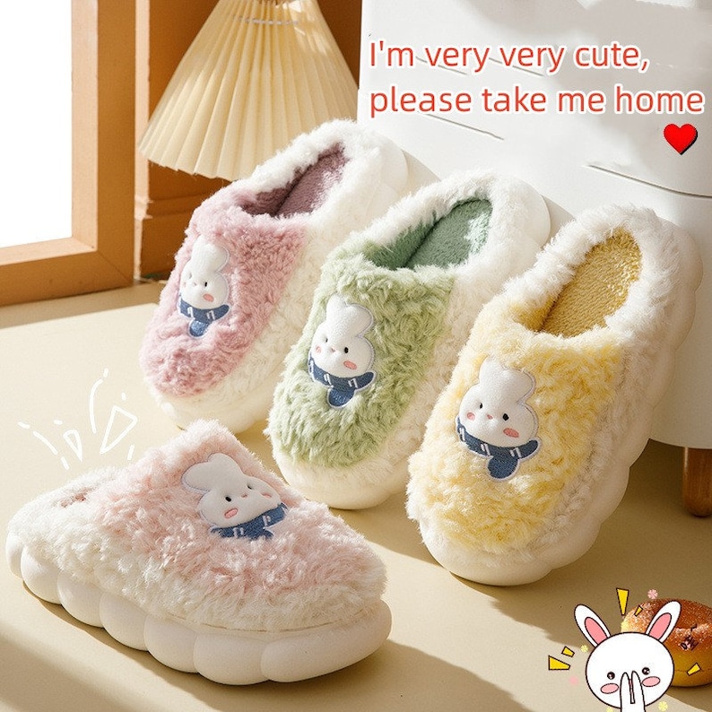 May include: Four pairs of fluffy house slippers in pastel colors: pink, green, white, and yellow. Each slipper features a cartoon bunny face and a thick, cushioned sole. The text "I'm very very cute, please take me home" is visible.