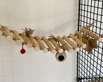 May include: A wooden bird toy for a cage, featuring a series of connected wooden dowels with rope and a small red bell hanging from one end. The toy also includes a cardboard tube and a small piece of cardboard with a hole in the center.