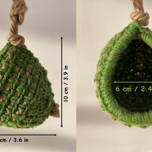 May include: A green and tan crocheted hanging pod with a jute rope hanger. The pod measures 3.9 inches in height and 3.6 inches in width, with a 2.4-inch wide opening. The structure is made of interwoven green and tan fibers in a textured pattern.