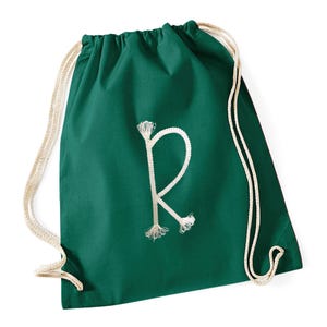 Puede incluir: Una mochila con cordón verde oscuro con una letra "R" blanca bordada en el centro. La bolsa tiene cordones de cuerda blancos. La bolsa está hecha de una tela suave.