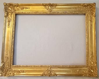 Könnte beinhalten: Ein verzierter Bilderrahmen in Gold mit einem dekorativen, geschnitzten Design. Der Rahmen ist aus Holz und hat eine glatte, glänzende Oberfläche.
