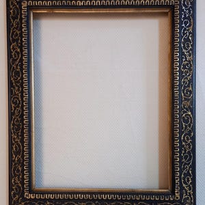 Pode incluir: Moldura retangular com um design ornamental preto e dourado. A moldura tem uma borda externa preta escura com arabescos dourados e uma borda interna dourada. A moldura está vazia, com um fundo branco visível através da abertura.
