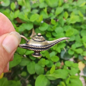 May include: A small, gold-colored genie lamp charm with intricate details. The lamp has a rounded base and a curved spout.