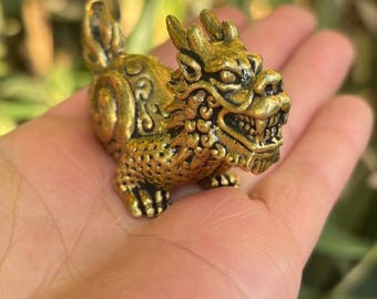 May include: A detailed, golden-colored figurine of a mythical creature, possibly a dragon or a similar beast. The sculpture has intricate details, including scales, claws, and a fierce expression. The figurine is held in a person's hand.