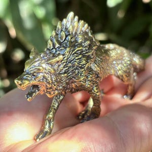 May include: A detailed brass wolf figurine with an open mouth, showcasing intricate fur and a spiky mane. The sculpture is in a walking pose, with a textured surface and a metallic gold color. The figurine is a decorative item.