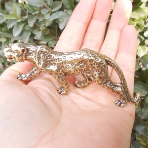 May include: A detailed, golden-colored leopard figurine. The sculpture features a spotted coat and is posed in a walking stance. The figurine is made of metal and has a detailed texture.