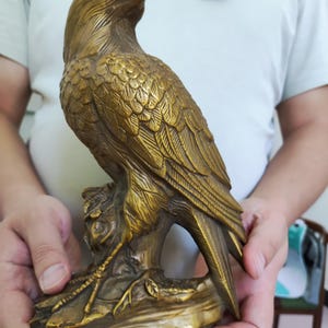 May include: A detailed bronze eagle sculpture perched on a branch. The eagle is depicted with intricate feather detailing and a focused gaze. The sculpture is a golden-brown color and appears to be made of metal.