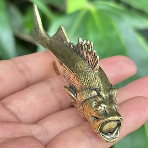 May include: A detailed bronze fish sculpture with textured scales, fins, and a prominent open mouth. The sculpture has a weathered, antique appearance, showcasing intricate details. The fish is a decorative item, possibly a figurine or a small statue.