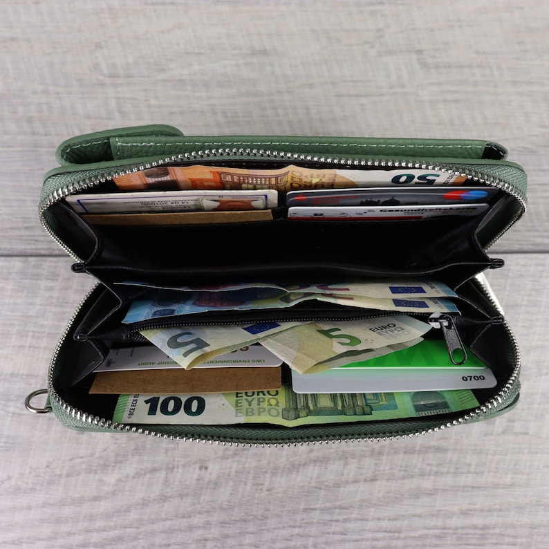 May include: A green leather zippered wallet with multiple compartments is open and filled with euro bills and credit cards. The wallet has a zipper closure and a small metal loop.