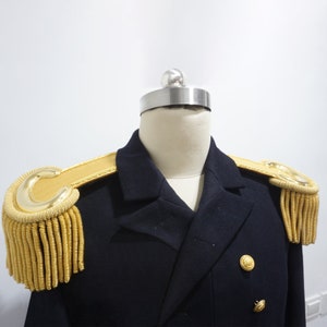 May include: A navy blue double-breasted jacket with gold shoulder boards and gold fringe. The jacket has two gold buttons.