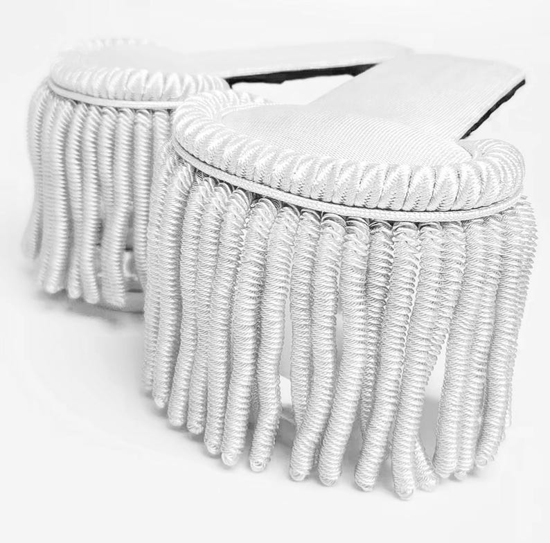 May include: White fringed trim with a decorative edge. The trim is made of a soft, white fabric and has a delicate, flowing fringe.