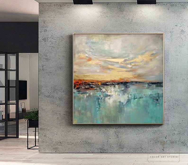 May include: Abstract landscape painting with a gold, orange, and teal color palette. The artwork features a textured sky and water reflection, framed in a gold-toned border. The painting is displayed on a gray wall.