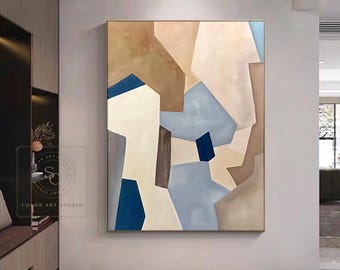 May include: A large rectangular wall art piece featuring an abstract composition of geometric shapes in shades of beige, tan, light blue, dark blue, and grey. The painting has a textured surface and is displayed in a thin, metallic frame.