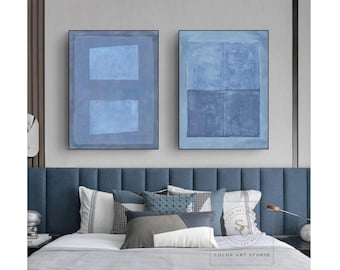 May include: Two rectangular wall art pieces featuring abstract blue geometric shapes. The left canvas displays two light blue rectangles on a darker blue background, while the right canvas shows a grid of four blue squares in varying shades.