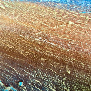 Puede incluir: Primer plano de una superficie de madera con un acabado de pintura texturizado y en capas. La superficie est&aacute; pintada en tonos de marr&oacute;n, azul y amarillo.
