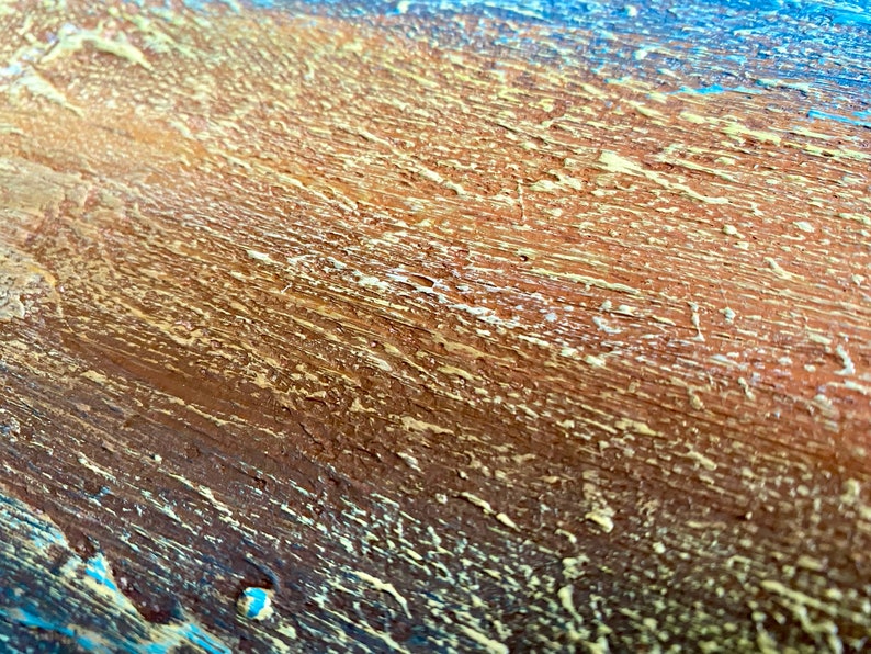 Puede incluir: Primer plano de una superficie de madera con un acabado de pintura texturizado y en capas. La superficie est&aacute; pintada en tonos de marr&oacute;n, azul y amarillo.
